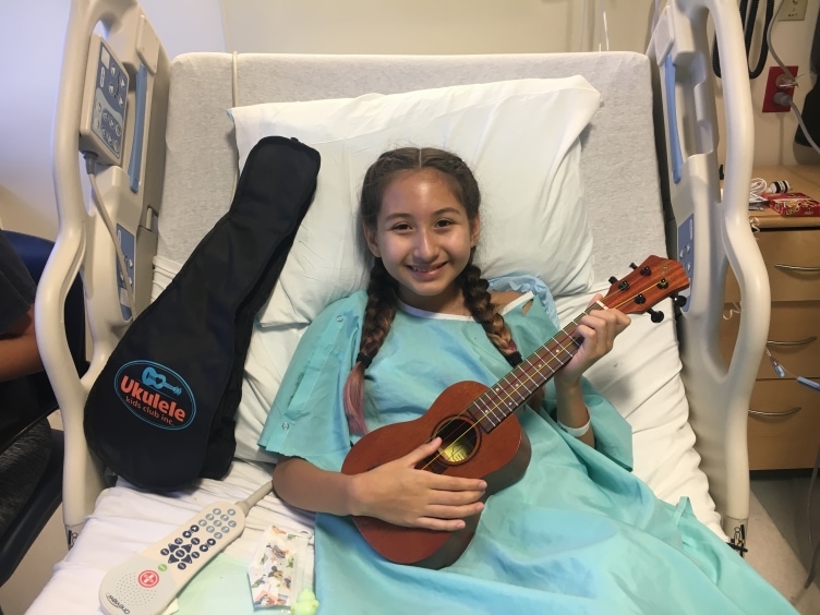 A child in a hospital bed with a UKC ukulele