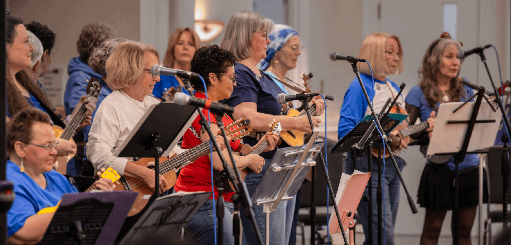 A group of women playing ukuleles and singing on stage.