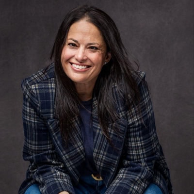 A portrait photo of Stacie Weisbrot sitting in a chair and leaning into the camera